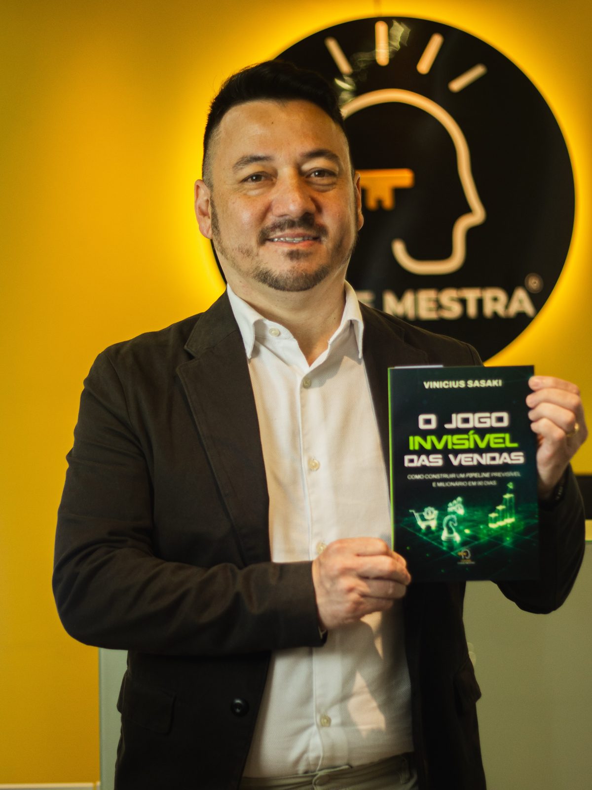 Vinicius Sasaki segura um exemplar de O Jogo Invisível das Vendas diante do logo da Editora Chave Mestra