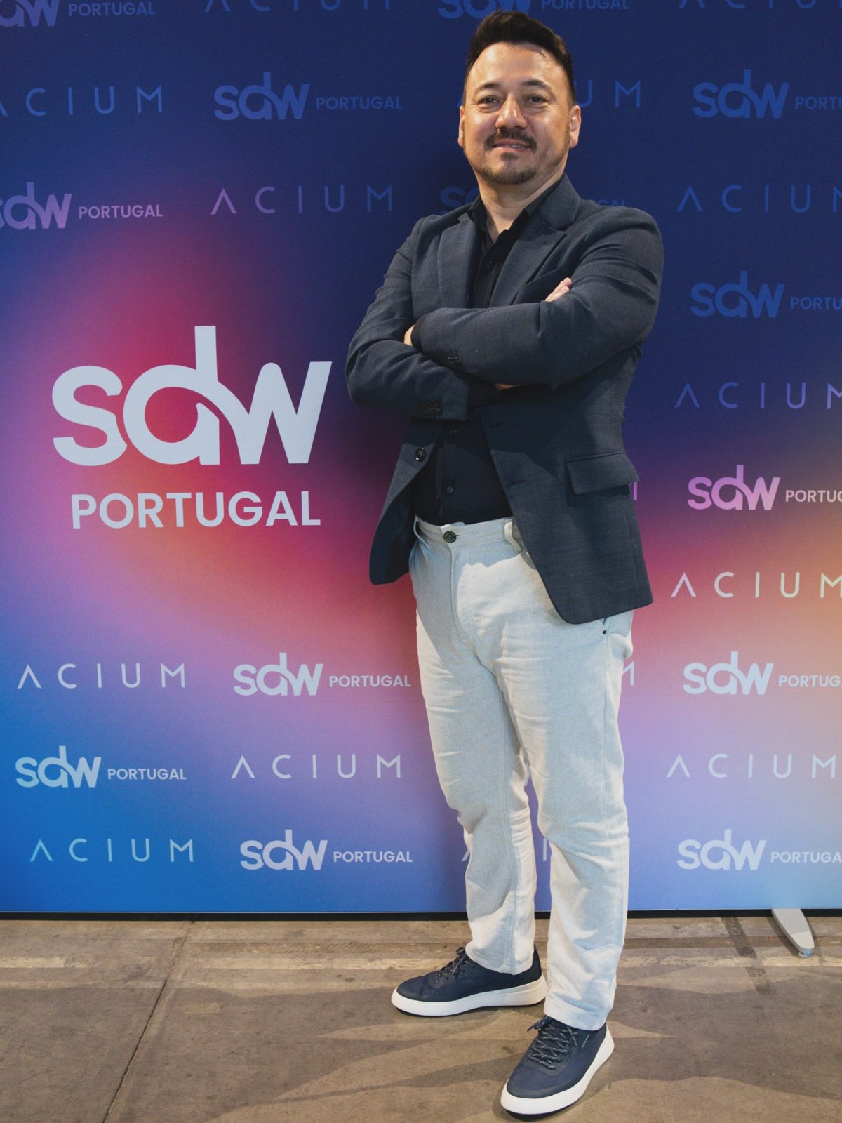 Vinicius Sasaki de braços cruzados diante do painel com a marca SDW Portugal