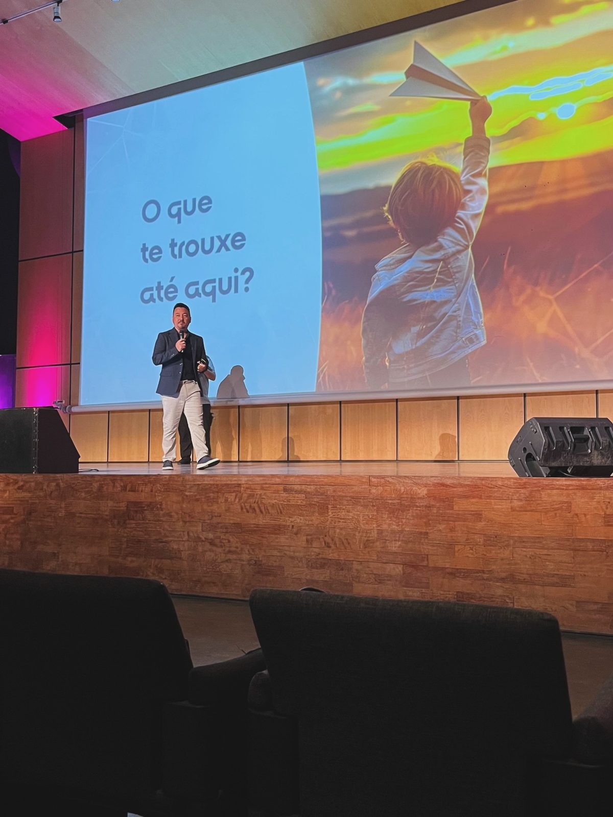 Vinicius Sasaki no palco do SDW Portugal; no telão, a pergunta “O que te trouxe até aqui?”