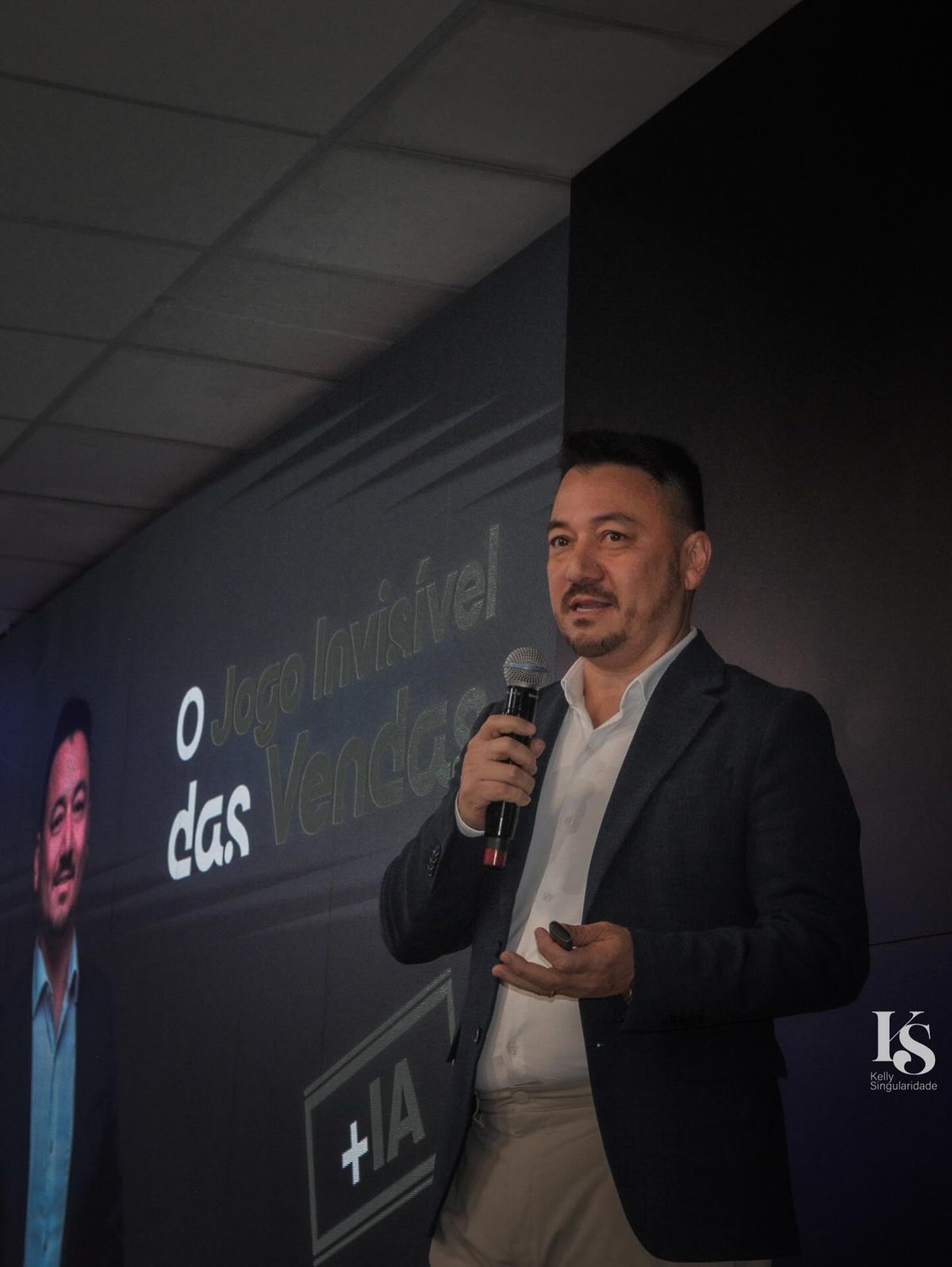 Vinicius Sasaki de microfone na mão diante do telão com o título O Jogo Invisível das Vendas